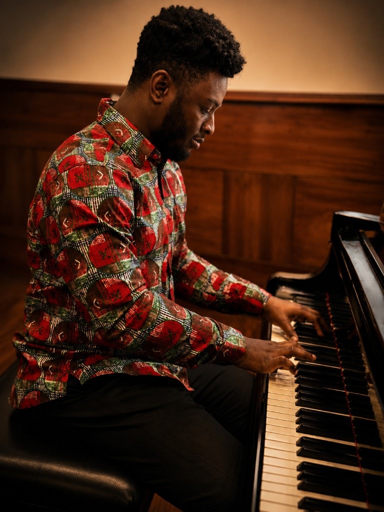 Ato Baah-Nyarkoh in African print shirt, playing piano in profile.
